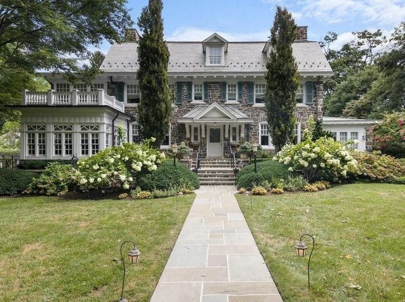 Stone house with a slate roof, symmetrical facade, and manicured landscaping, leading up a stone path.
