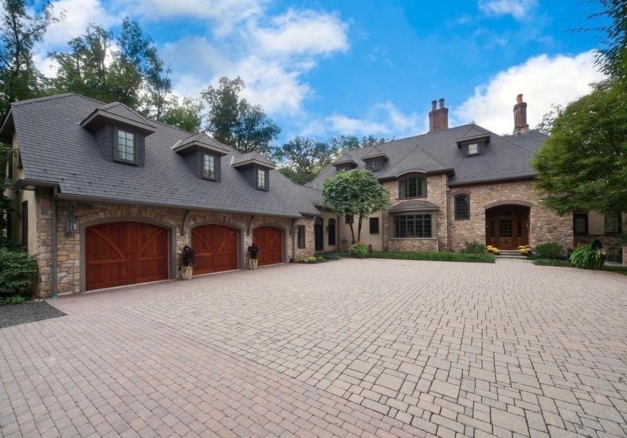 Brick mansion with three-car garage, red doors, and brick driveway on a sunny day.