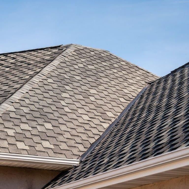 Gray asphalt shingle roofs on a house against a clear blue sky.
