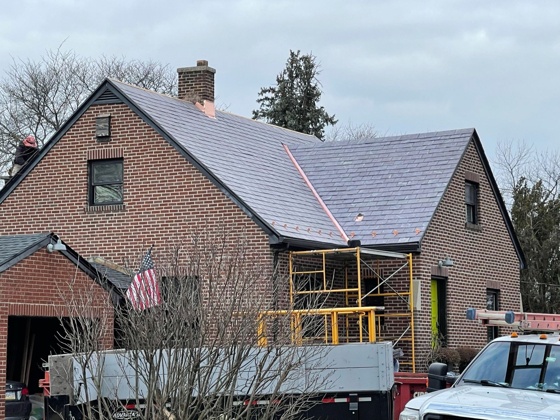 Brick house with new gray roof, scaffolding, and a utility truck.