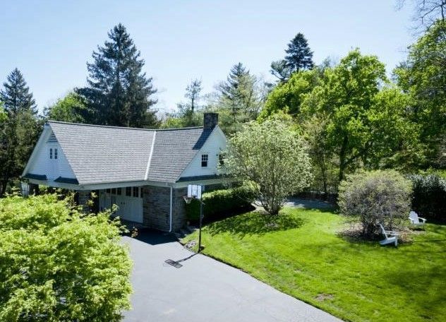 House with a gray roof and driveway, surrounded by green trees and grass on a sunny day.