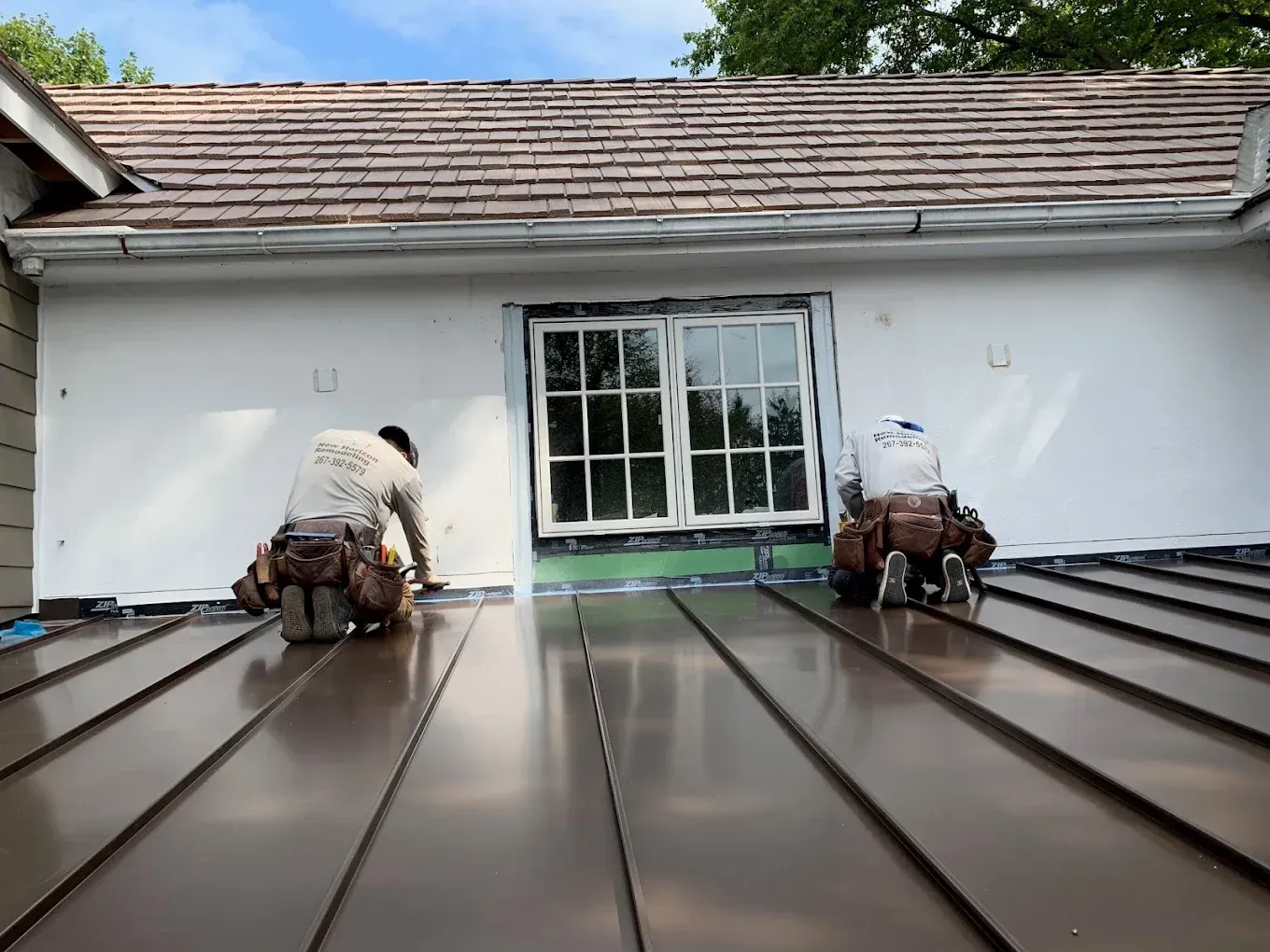 Two roofers installing copper metal roofing on a residential building.