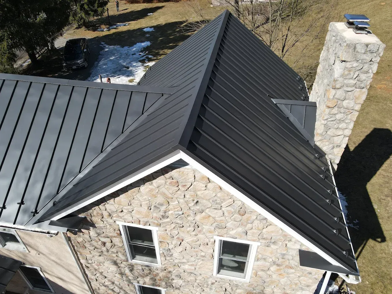 Black metal roof on a stone house with a stone chimney.