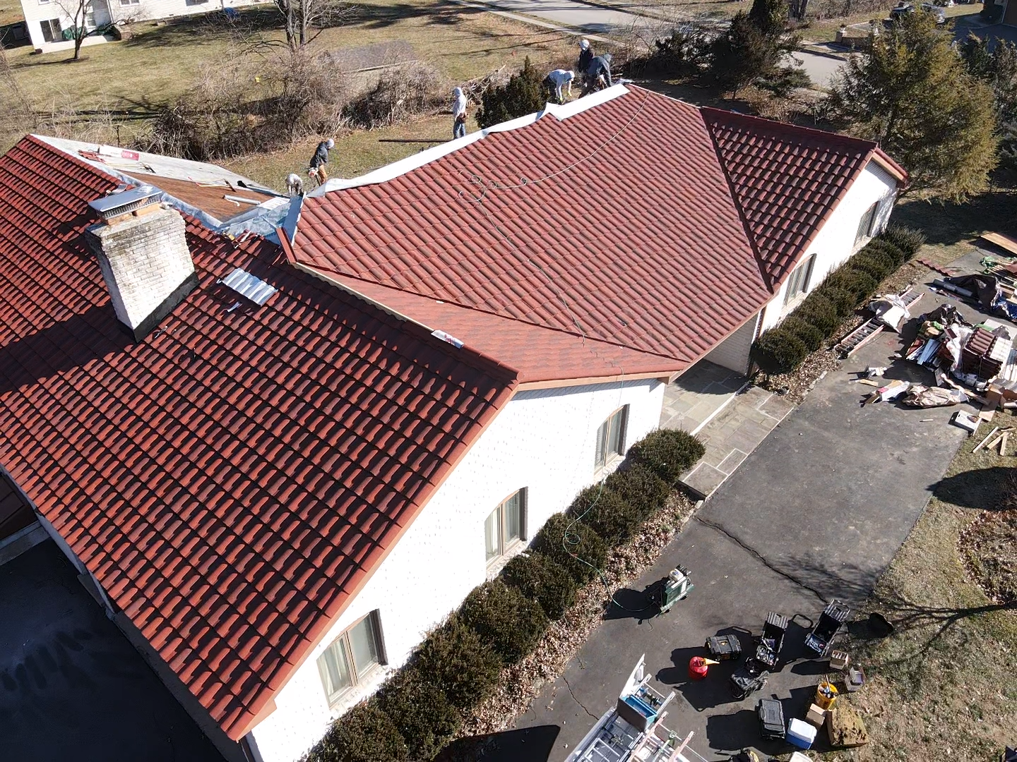 Red tile roof being worked on by several people. White building, sunny day.