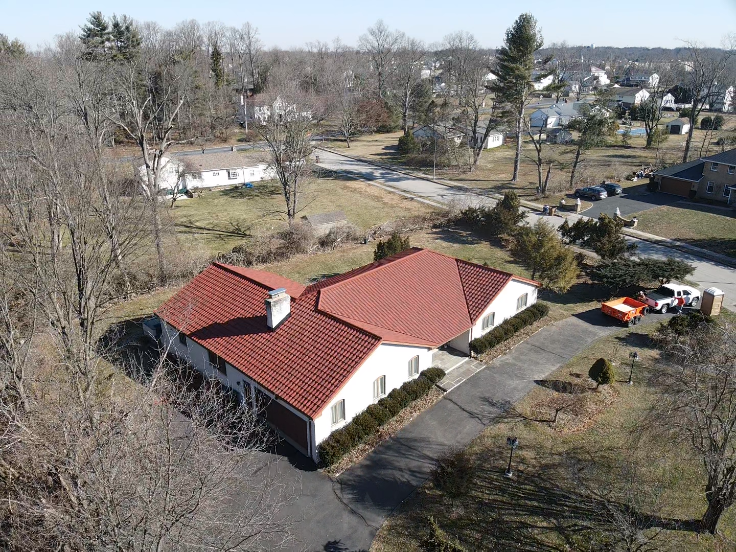 Overhead view of a house with a red-tiled roof, set in a neighborhood with bare trees and a driveway.