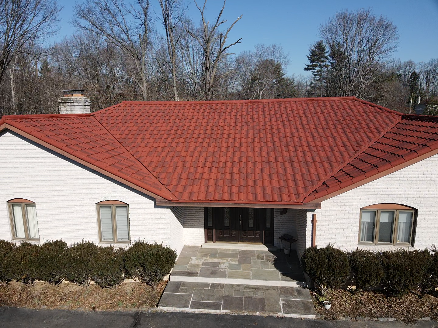 White house with red tile roof, stone steps leading to front door, bushes, and bare trees.