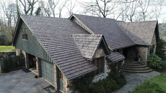 Stone and wood house with a gray shingled roof, built-in garage, and steps leading to the entrance.