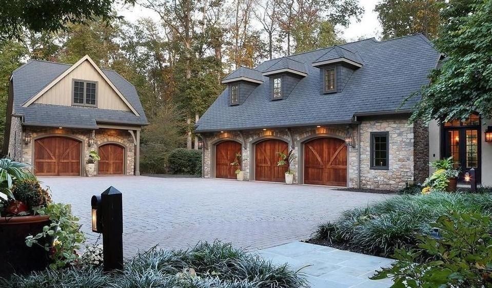 Stone garages with wooden doors, a brick driveway, and landscaping.