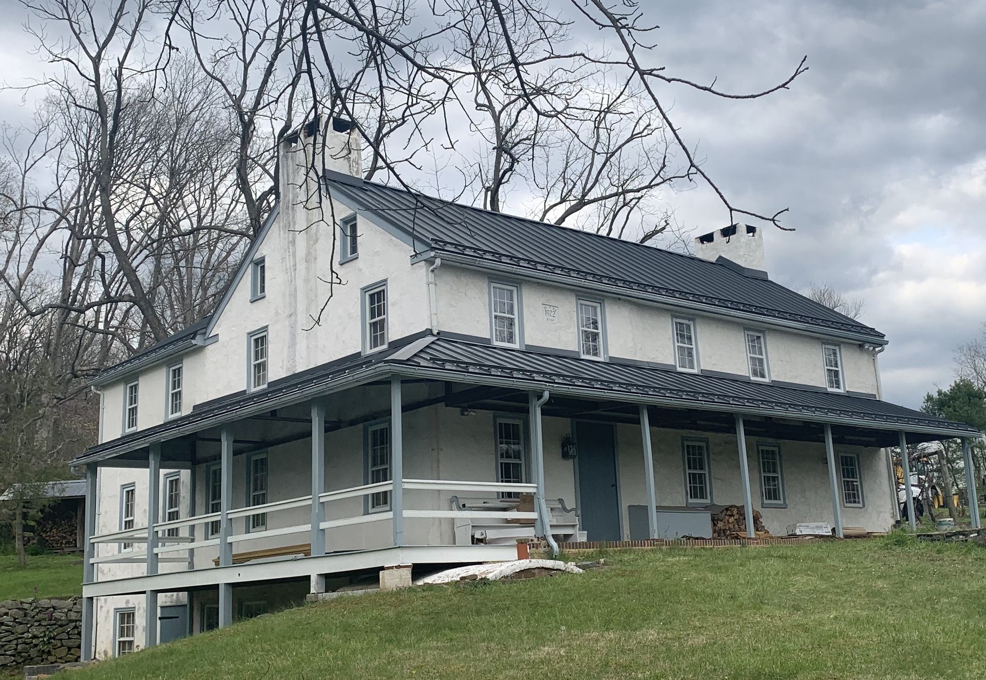 White two-story house with a wraparound porch, blue roof, and a grassy yard.