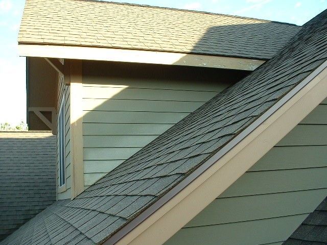 Roofs with brown shingles meet light green siding under a blue sky.