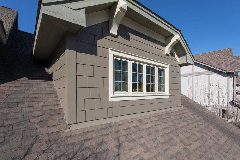 Grey roof with window, gray siding, and decorative brackets, against a clear blue sky.