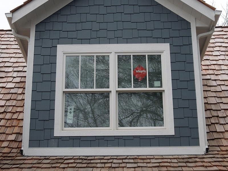 Dormer with a white-framed window on a building with blue siding and cedar shake roof.