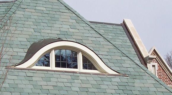 Dormer window with arched top on a green shingle roof. White trim, three pane window.