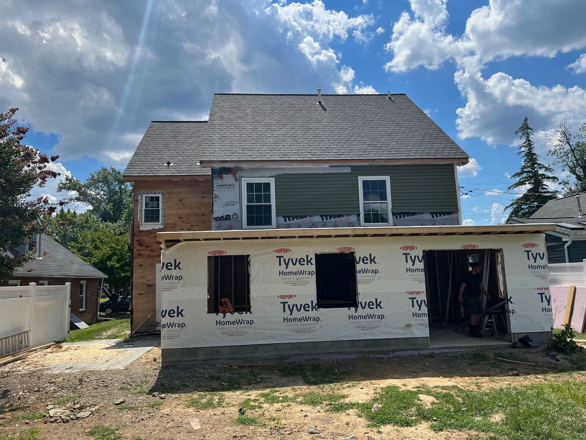Construction site: two-story house under renovation, with exposed framing, green siding, and a partially built addition.