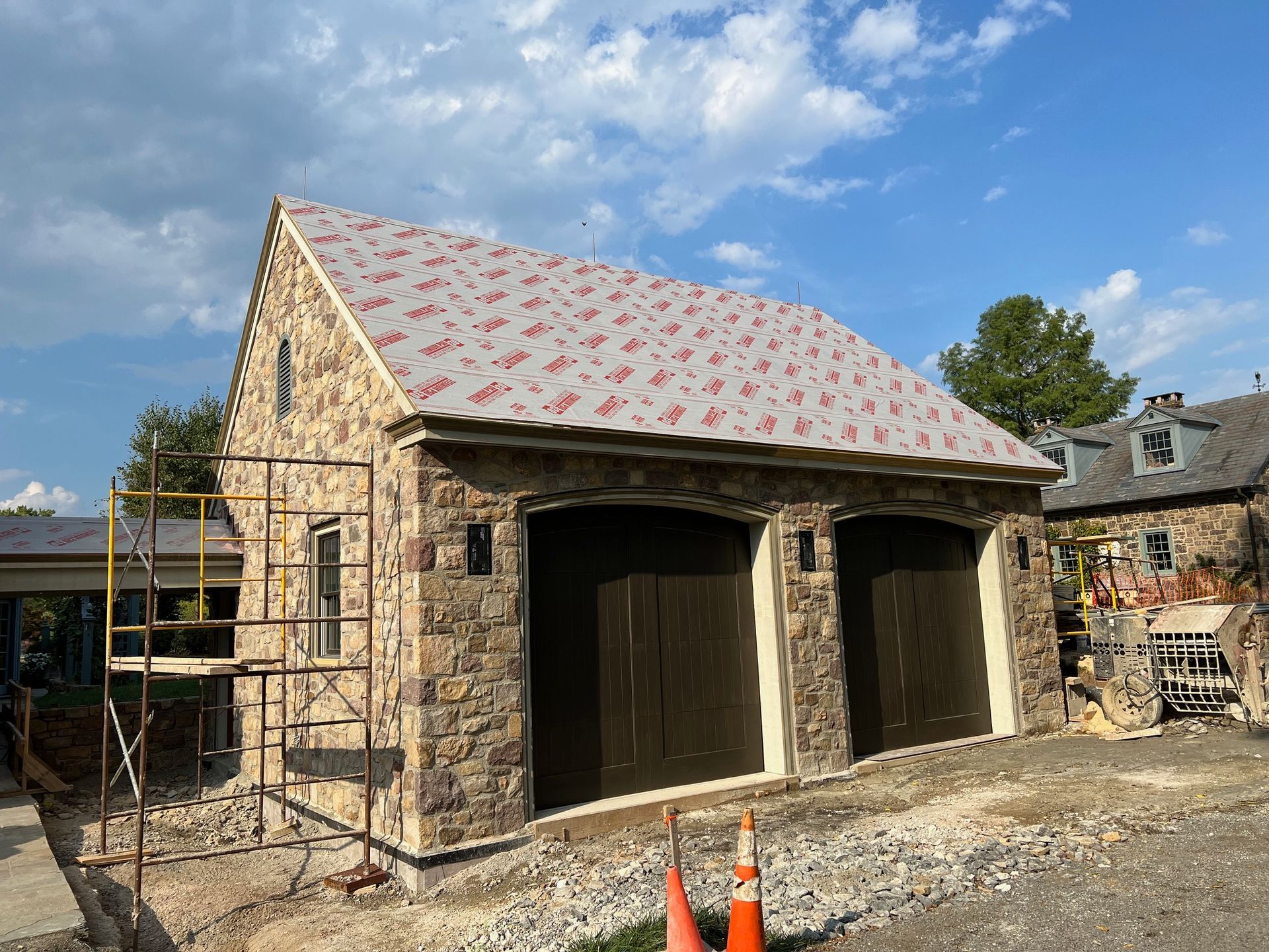 Stone garage with brown doors; scaffolding and roofing work in progress.