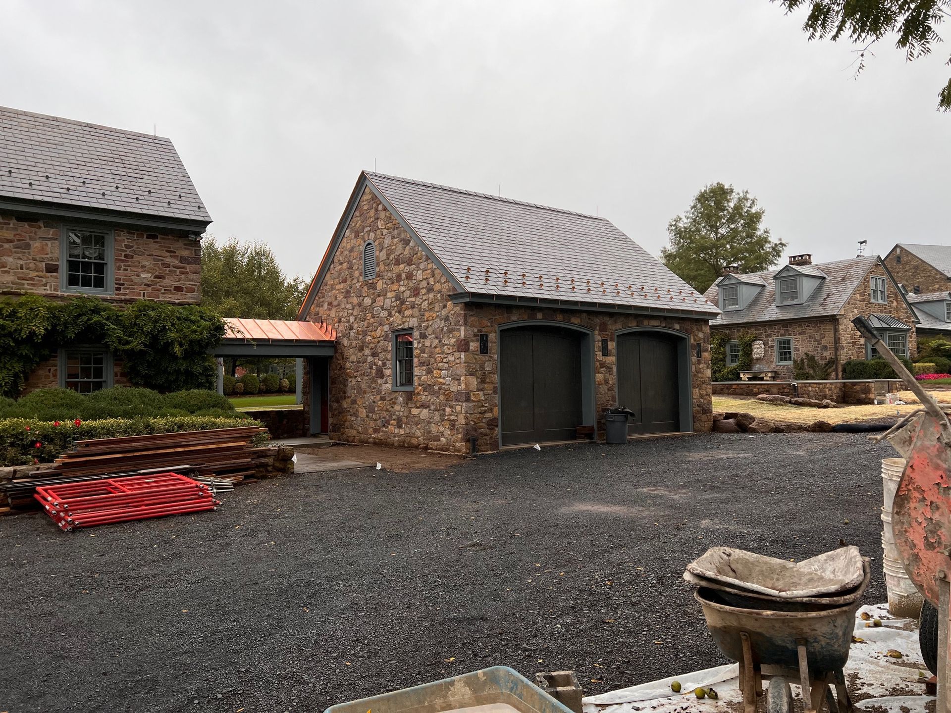 Stone buildings with gray metal roofs; a two-car garage, driveway, and landscaping in progress.