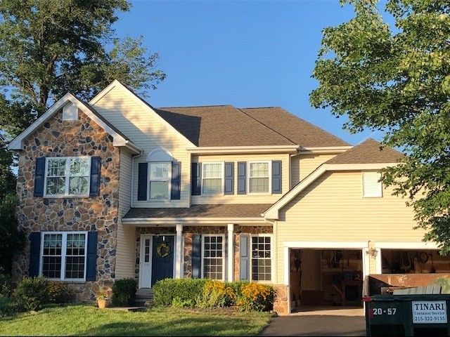 Two-story house with stone and beige siding, blue shutters, and open garage, under a blue sky.