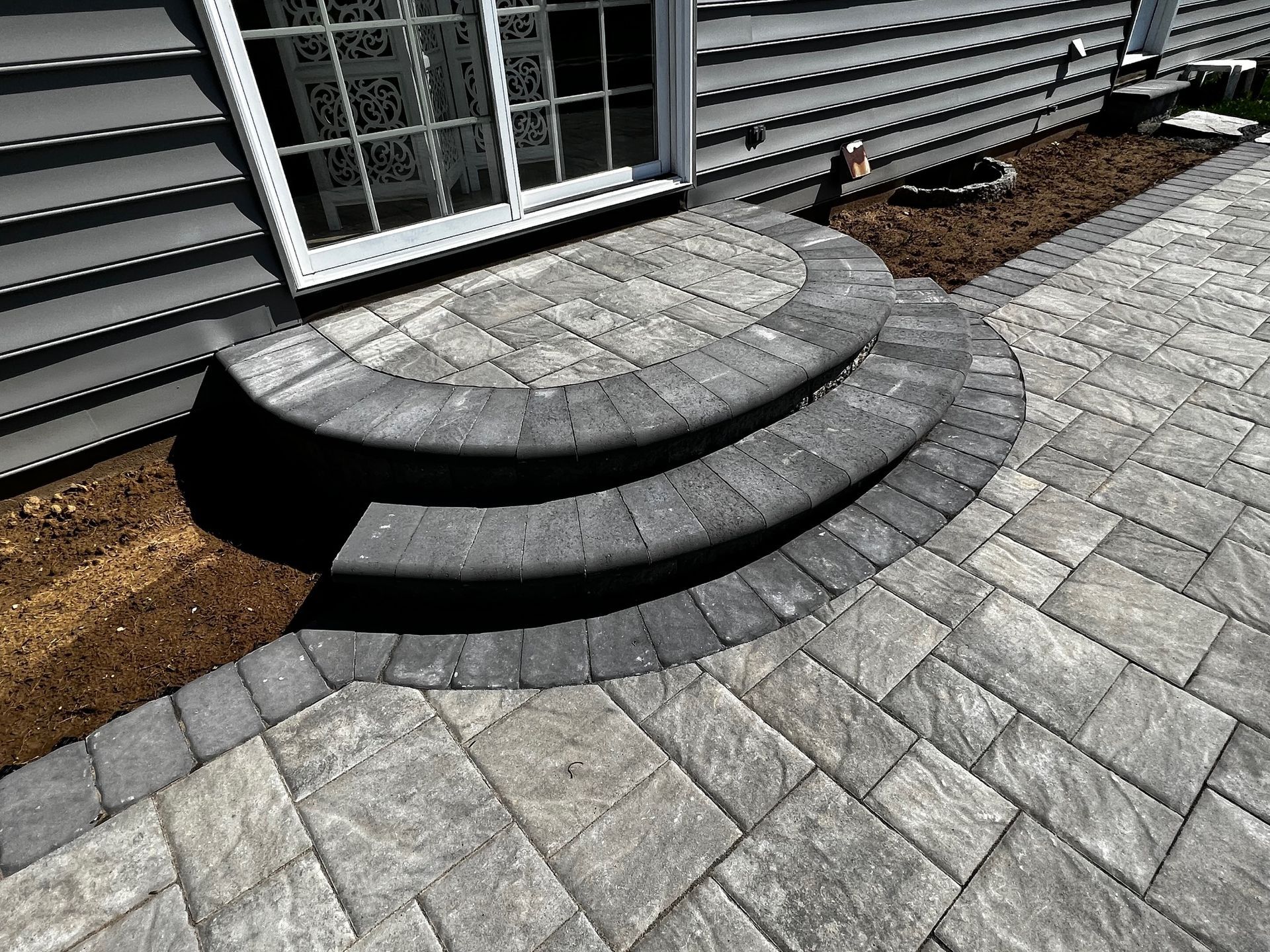 Stone steps leading up to a door with a matching paved patio. Grey siding.