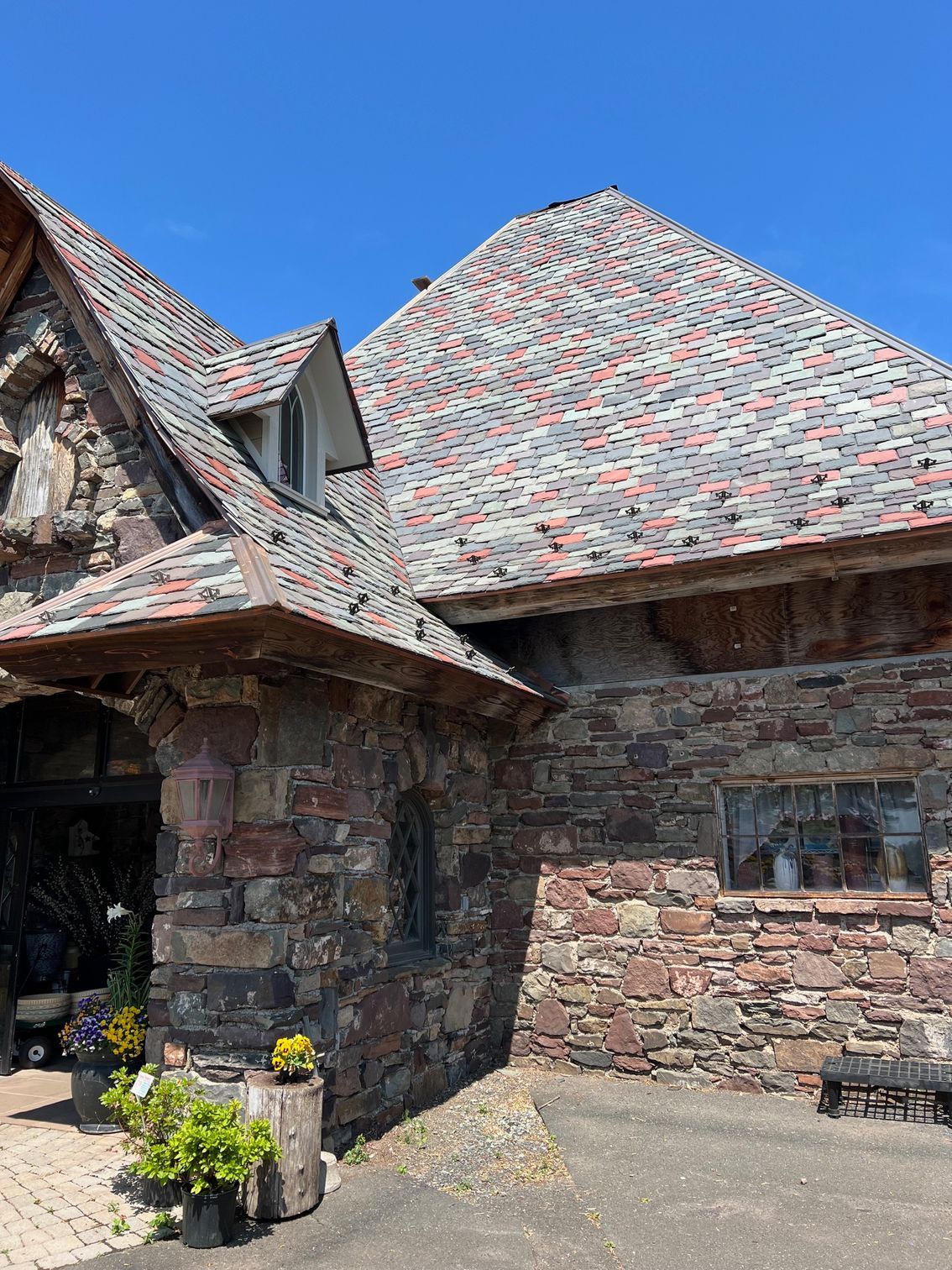 Stone building with red-grey tiled roof, arched entrance, and small window under a blue sky.