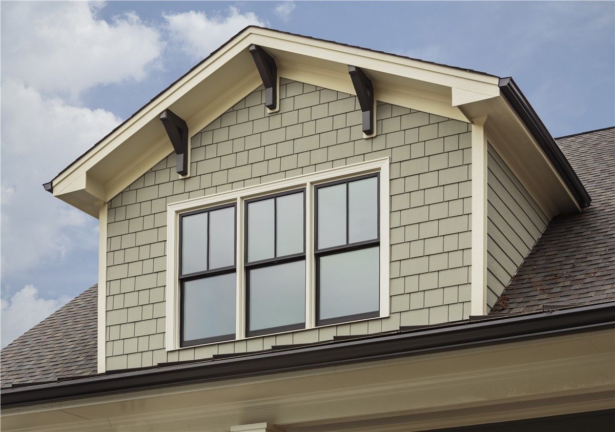 Dormer window with three panes, green siding, and brown roof. Beige trim and support brackets.