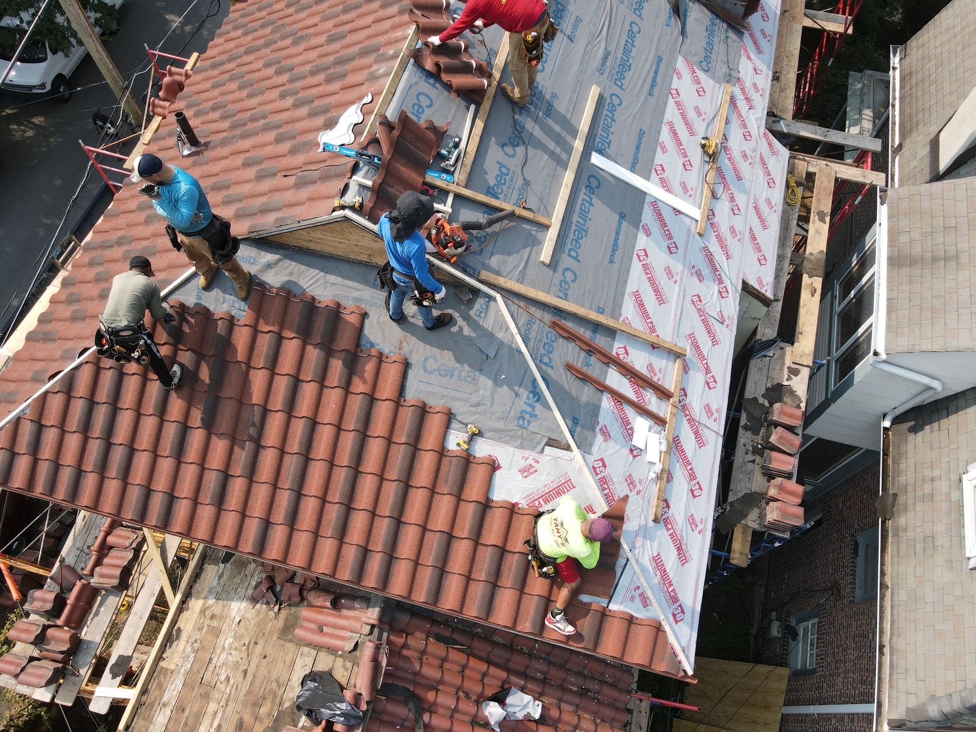 Roofers installing clay tiles on a house. Workers in action, wearing safety gear. Setting is outdoors.