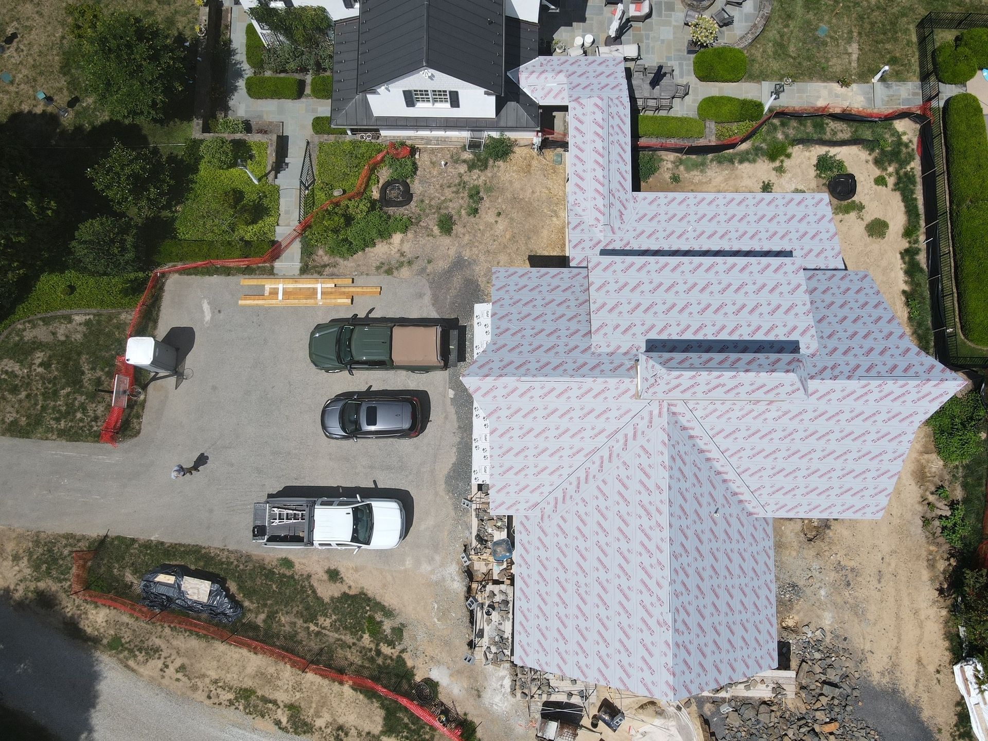 Aerial view of a house under construction with a new roof and several vehicles parked nearby.