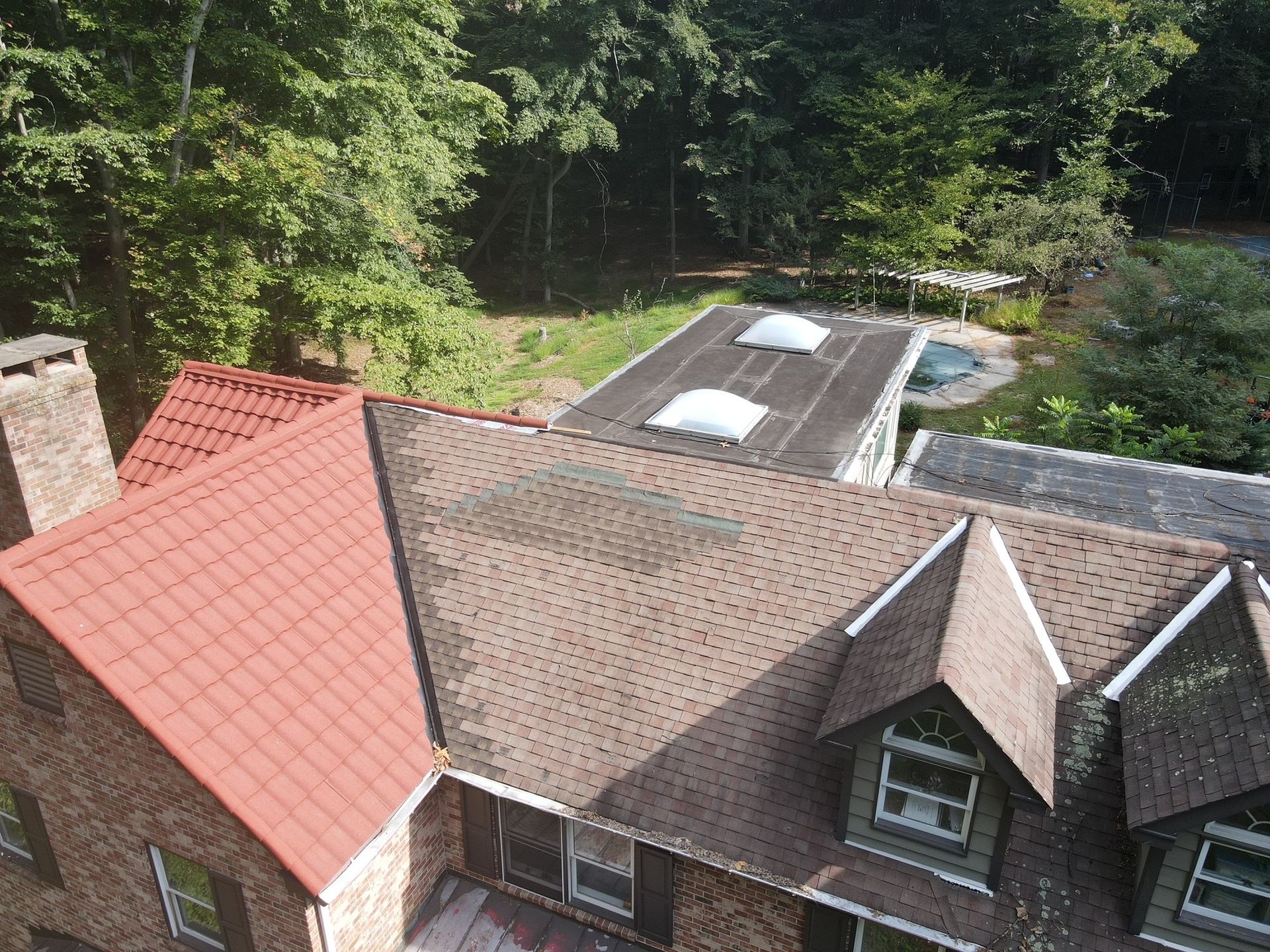 View of a multi-roofed brick building with different colored roofing surrounded by green trees.