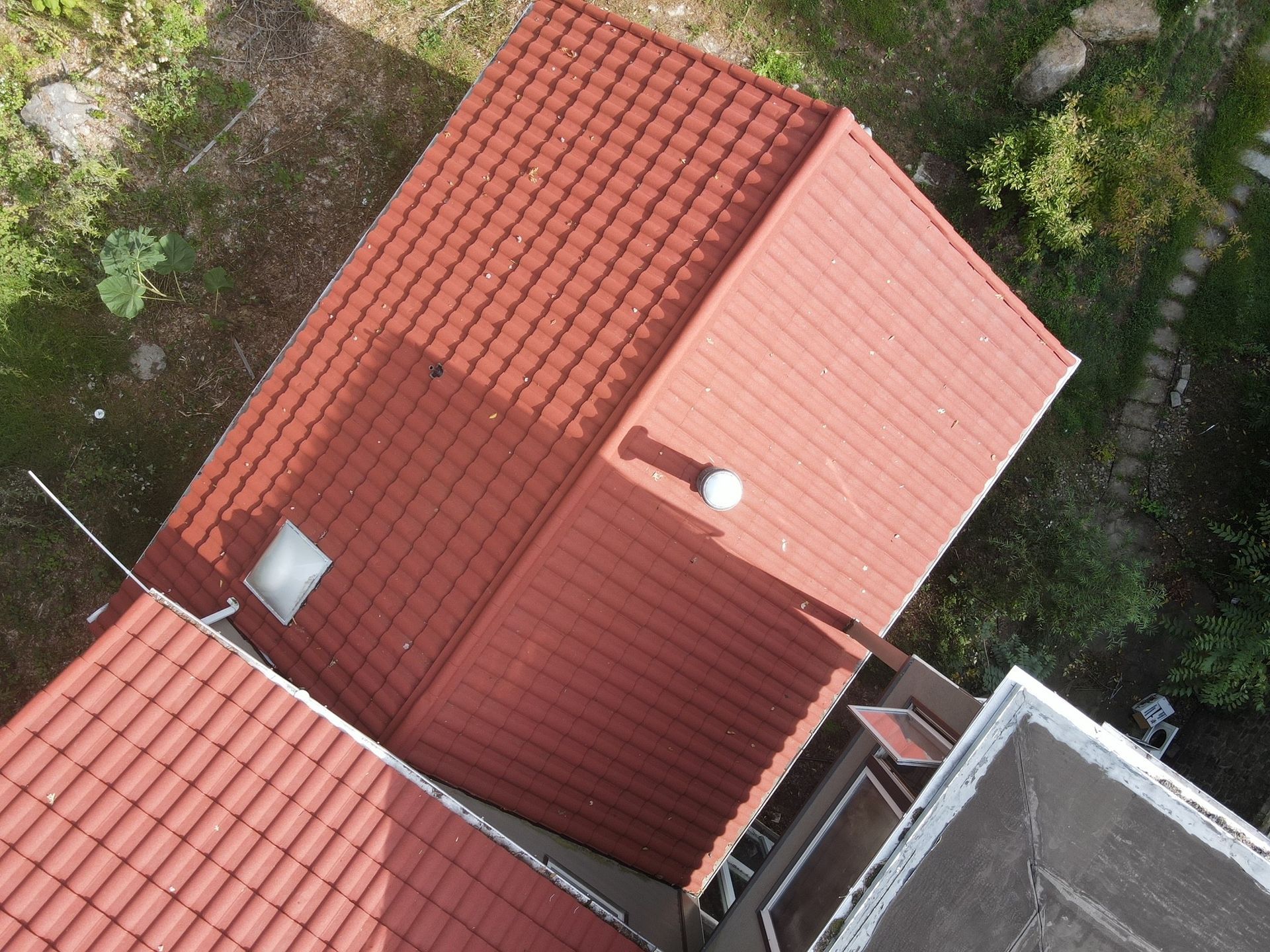 Overhead view of a house with a red tiled roof, surrounded by vegetation.