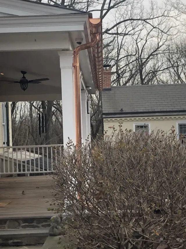 Copper guttering on a porch with a white column, overlooking a yard and trees.