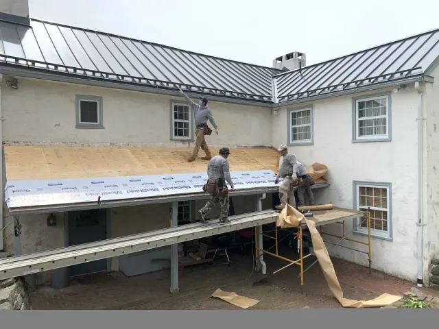 Roofers working on a house with a metal roof. Scaffolding supports the workers.