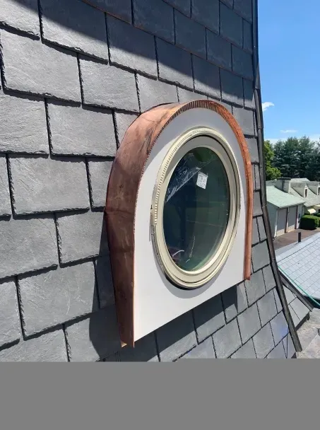 Round window on a slate roof, copper trim, white frame. Sunny day.