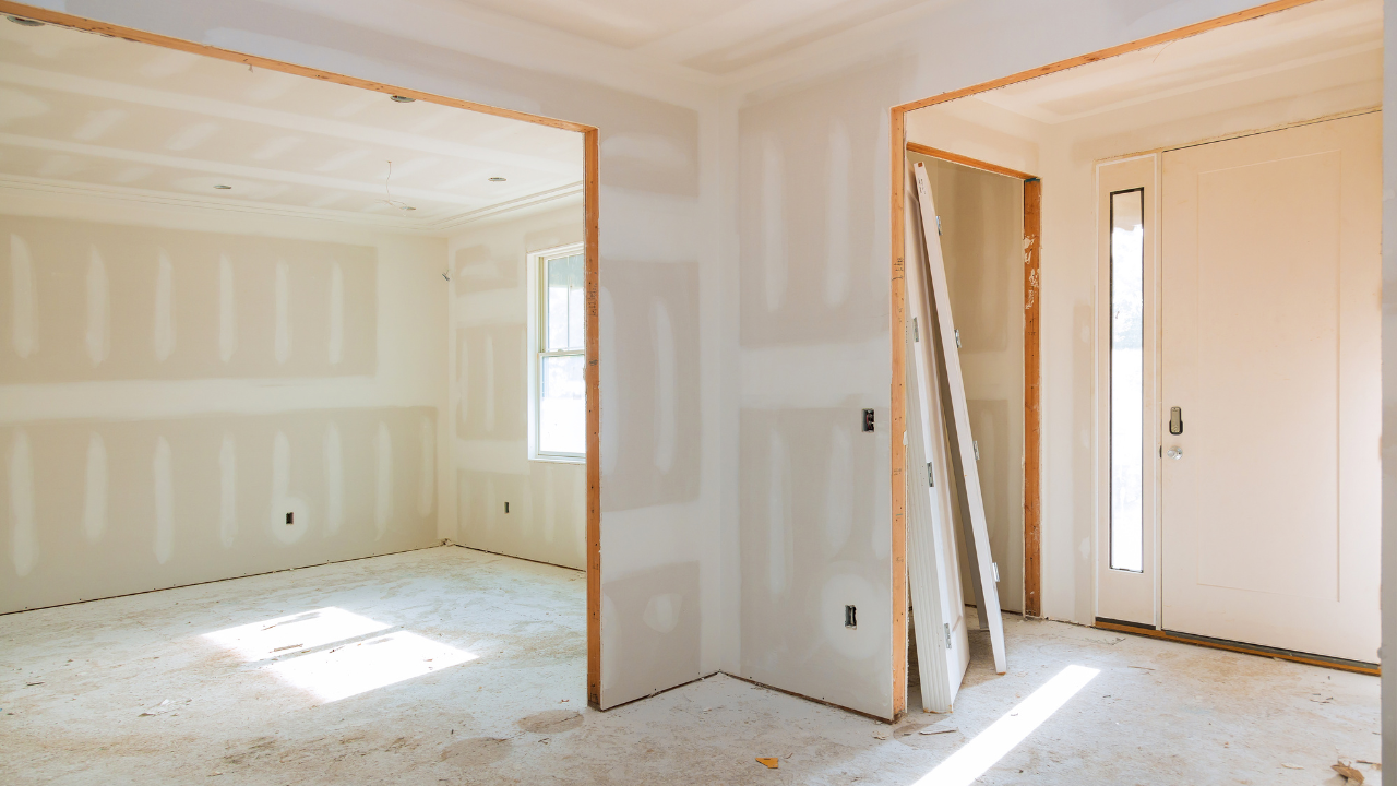 Interior of a room under construction, with drywall, wood frames, and sunlight.