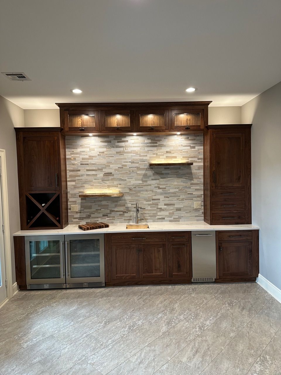 Built-in dark wood bar with wine storage, cabinets, a sink, and stone accent wall.
