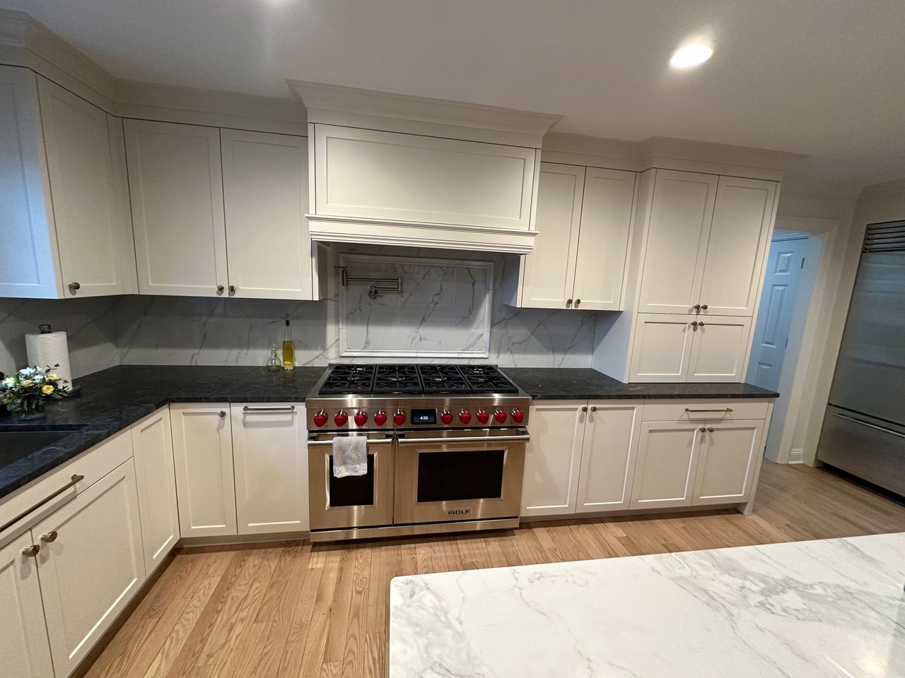 Kitchen with white cabinets, stainless steel range, dark countertops, and wood flooring.