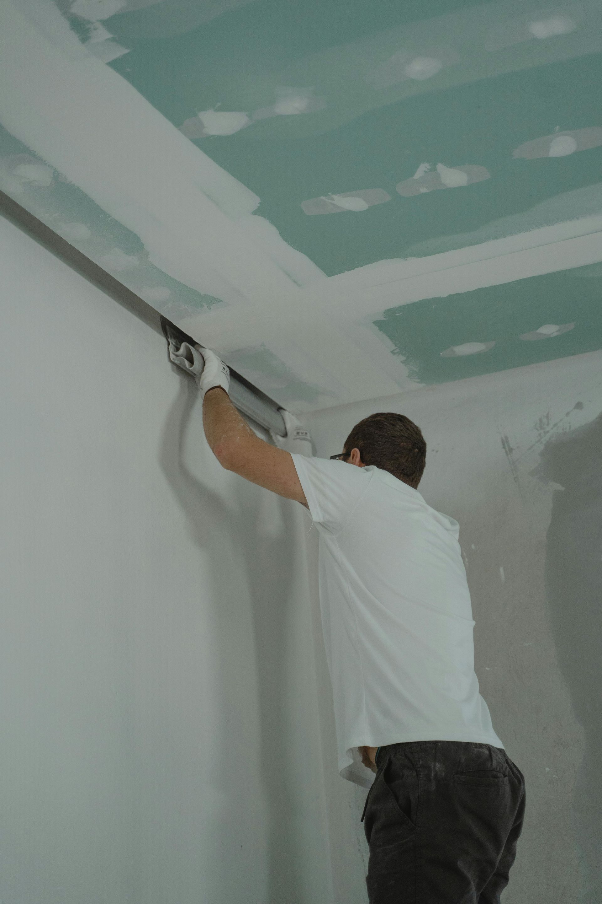 Person using a drywall knife to smooth joint compound where wall meets ceiling. Interior shot.