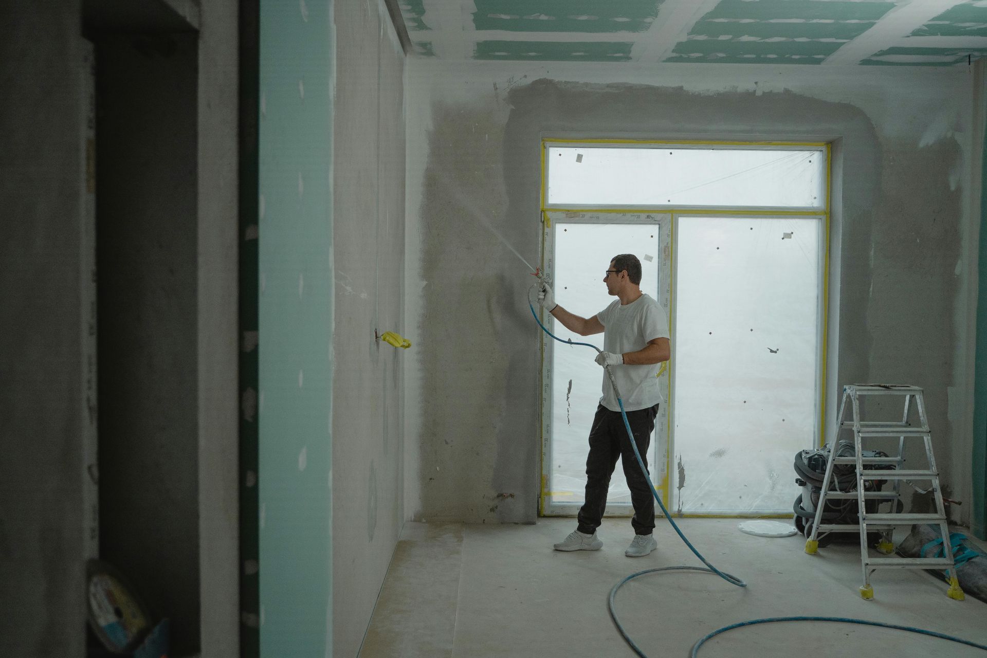 Man sprays plaster on a wall inside a room under construction.