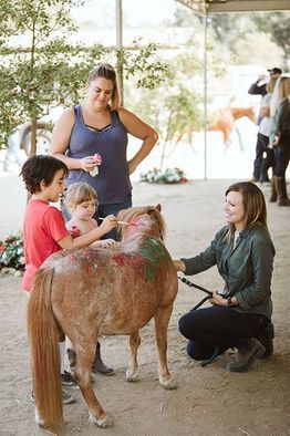 People petting a small brown pony in a barn-like setting