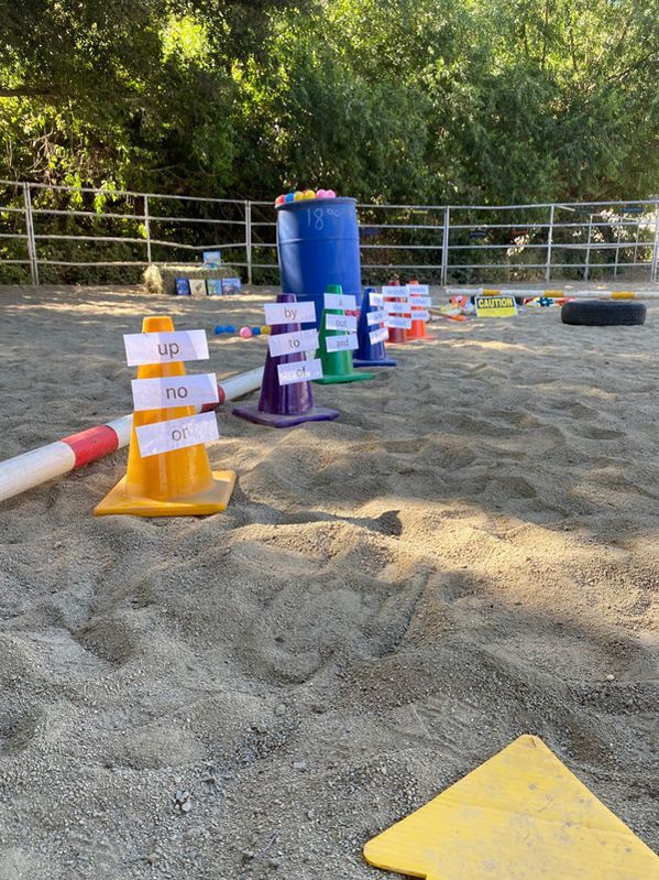 Colorful cones and numbered markers on a sandy outdoor field, with trees and a railing in the background