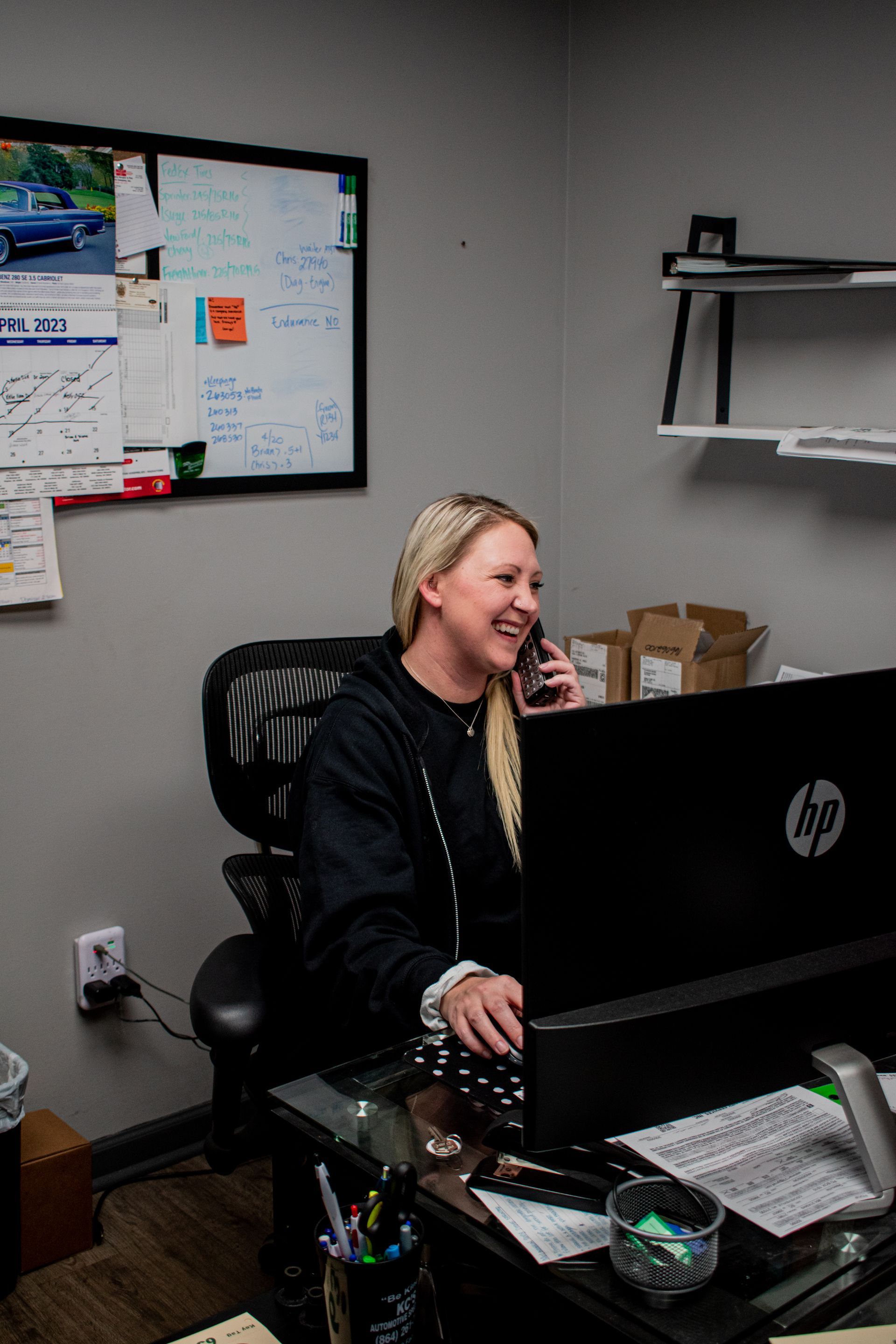 Woman smiling while on phone, seated at a desk in an office setting.