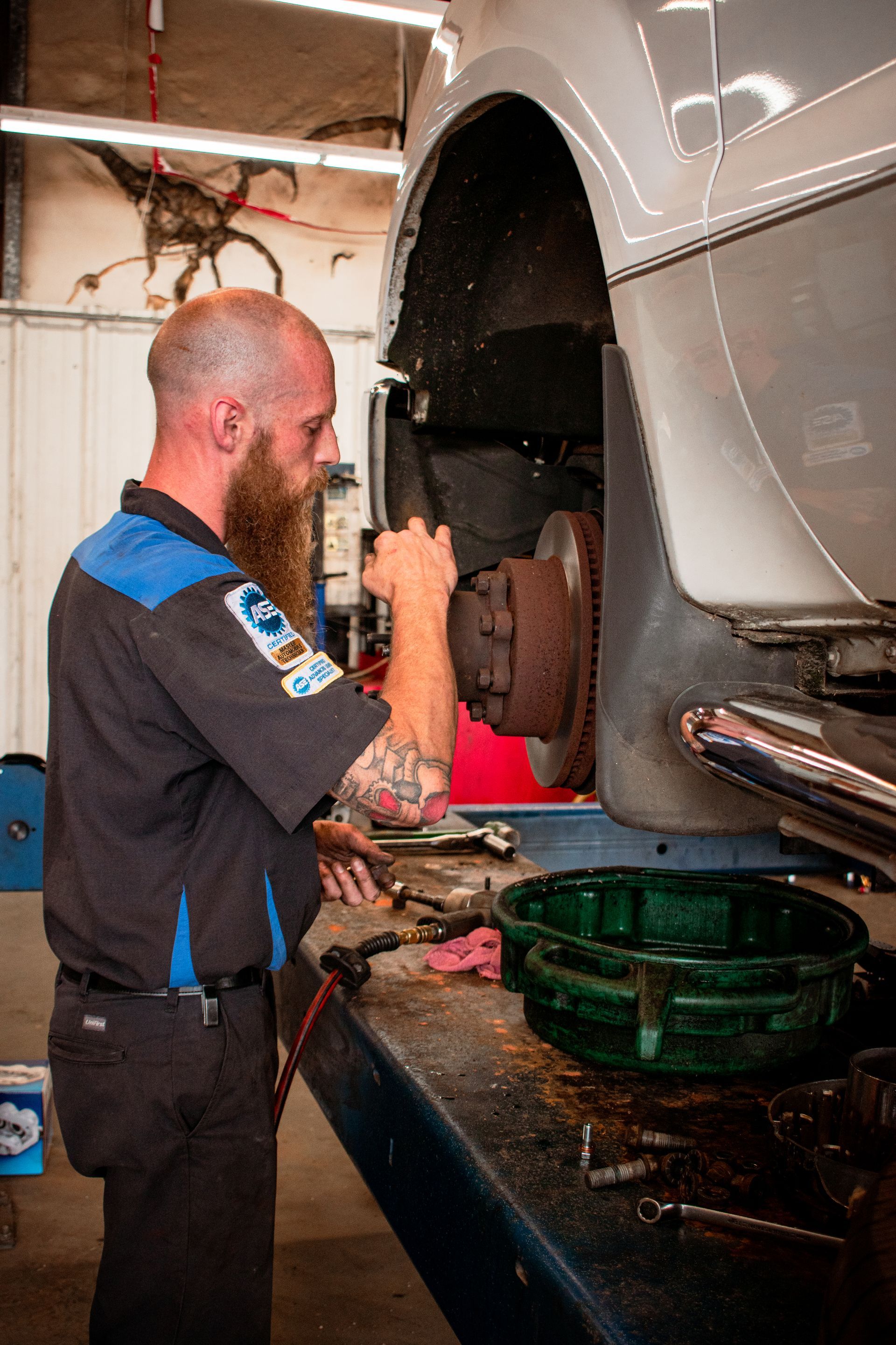 Mechanic working on car brake, wearing work shirt, in a shop.