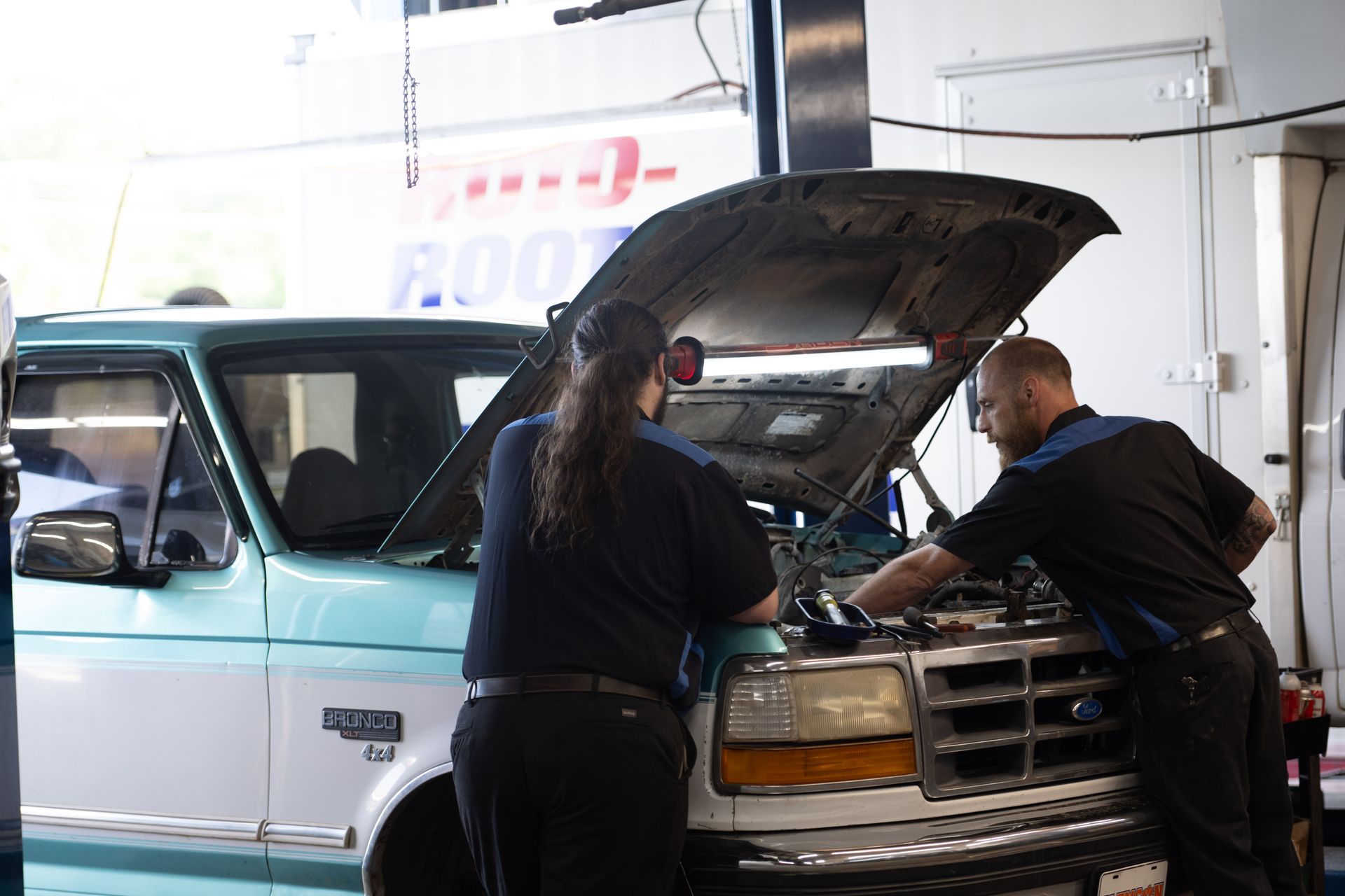 Two mechanics working on a truck engine in a garage; one has the hood open.