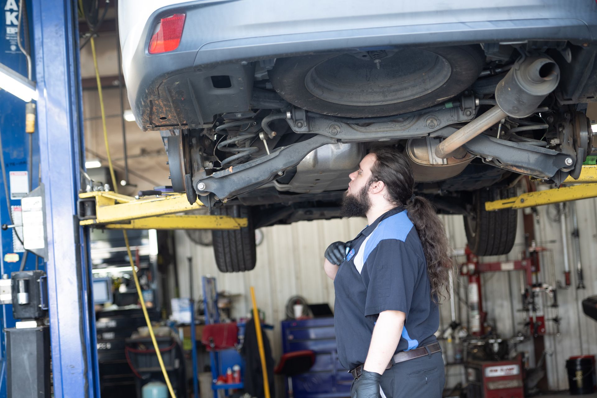 Mechanic inspecting the underside of a car on a lift in a garage.
