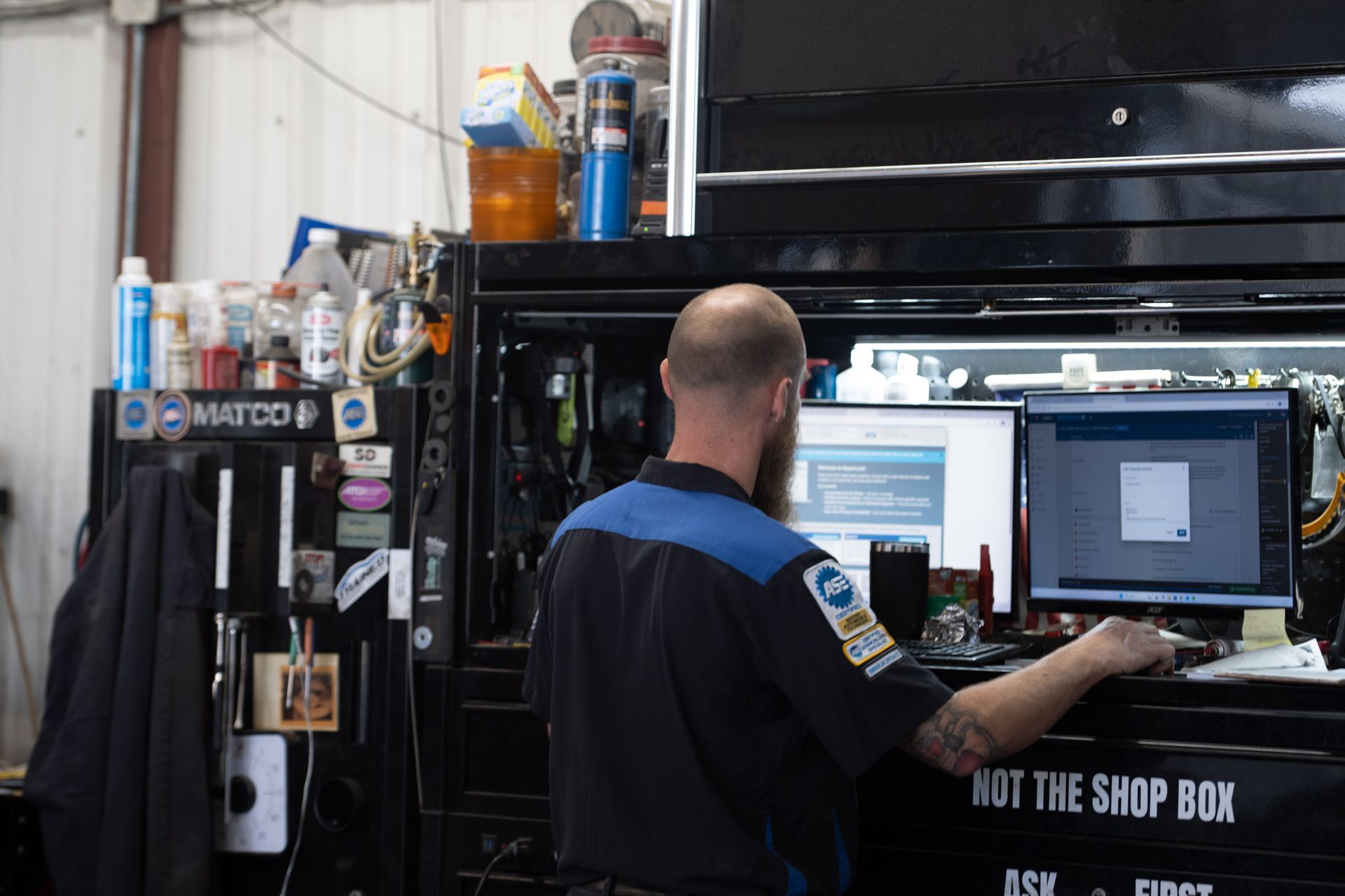 Mechanic at computer in garage, working on vehicle diagnostics.