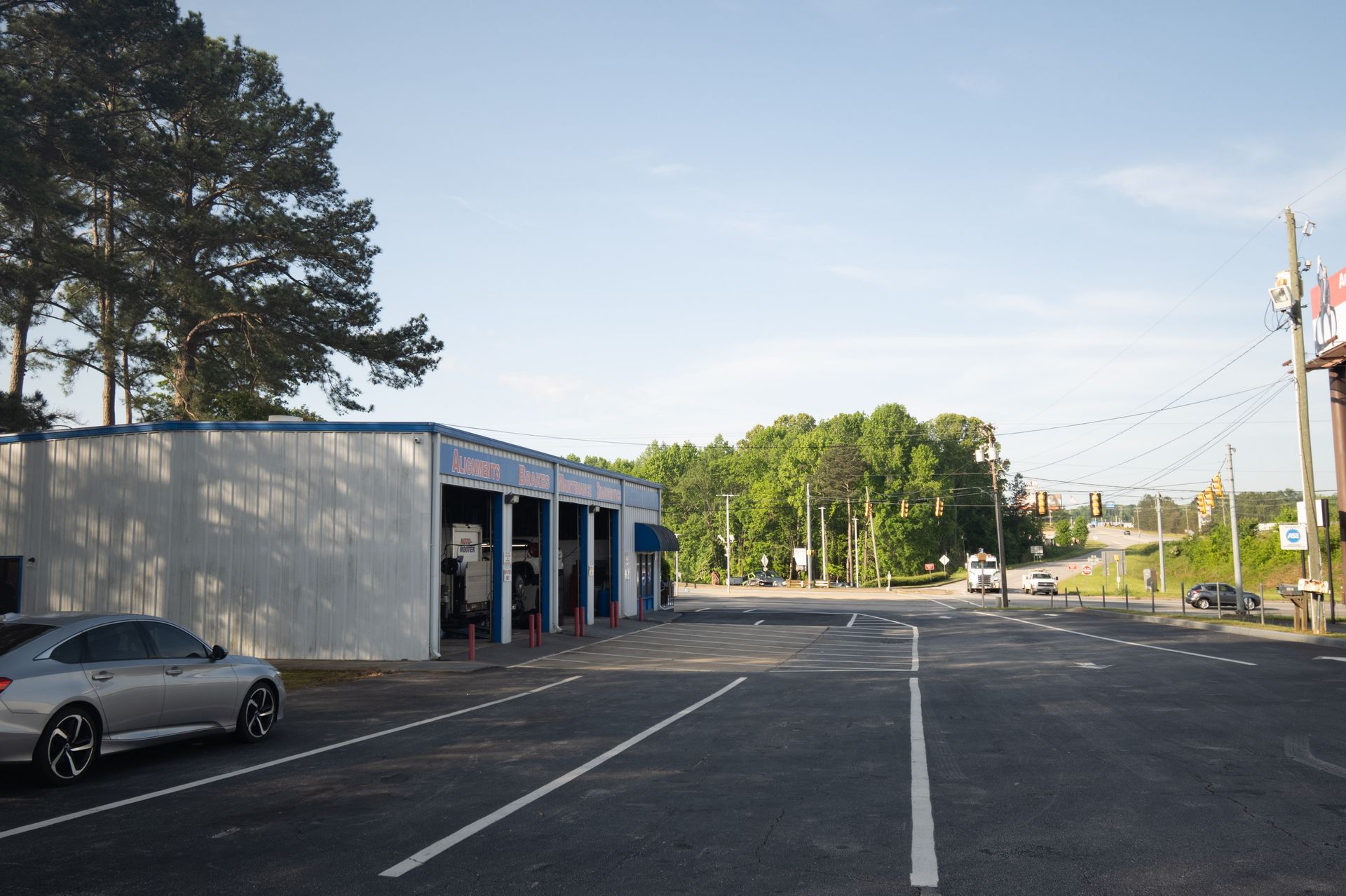 A tire shop with bays, a parked car, and a road. Clear sky, green trees.