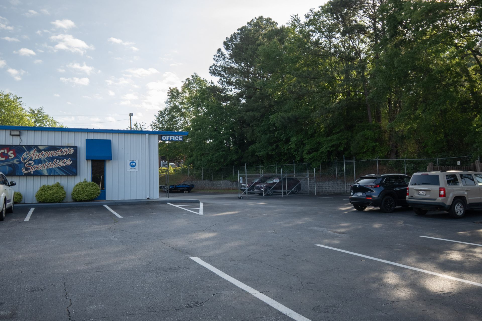 Parking lot in front of a blue and white building, with a few parked cars, and trees in the background.