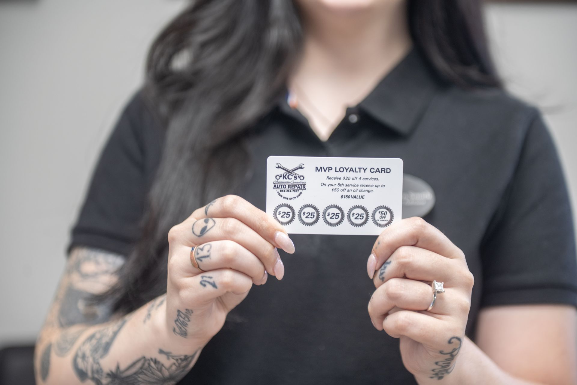 Woman holding a white card. The card has a logo and circles with numbers. The woman wears a black shirt and has tattoos.