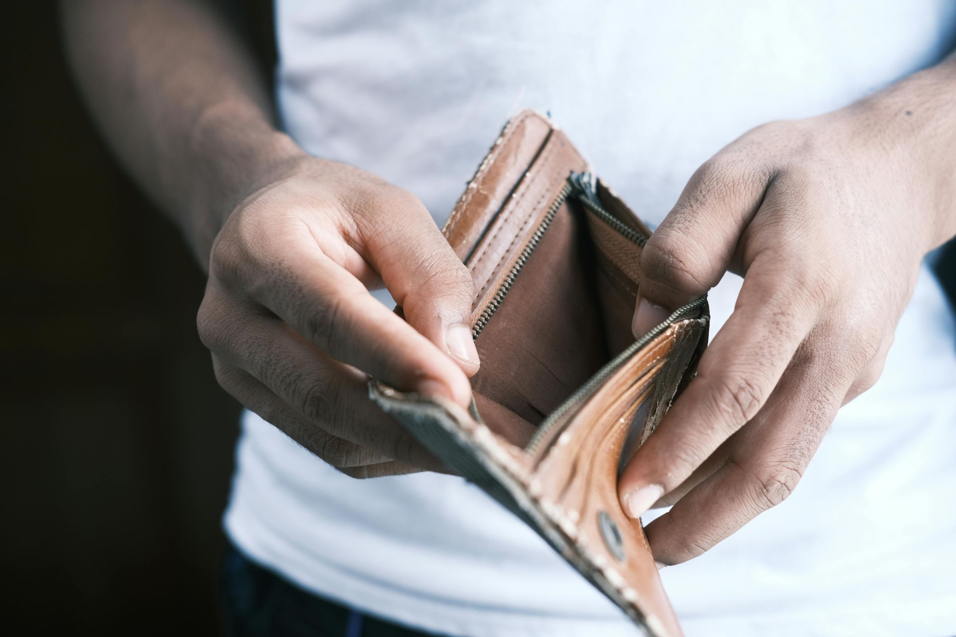 Person holding an empty brown wallet, indicating financial hardship.