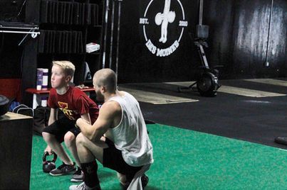 Two people kneel on a gym mat in Urbandale, IA, facing each other during a training drill.
