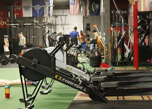 Indoor gym with a rowing machine in the foreground and people exercising in the background