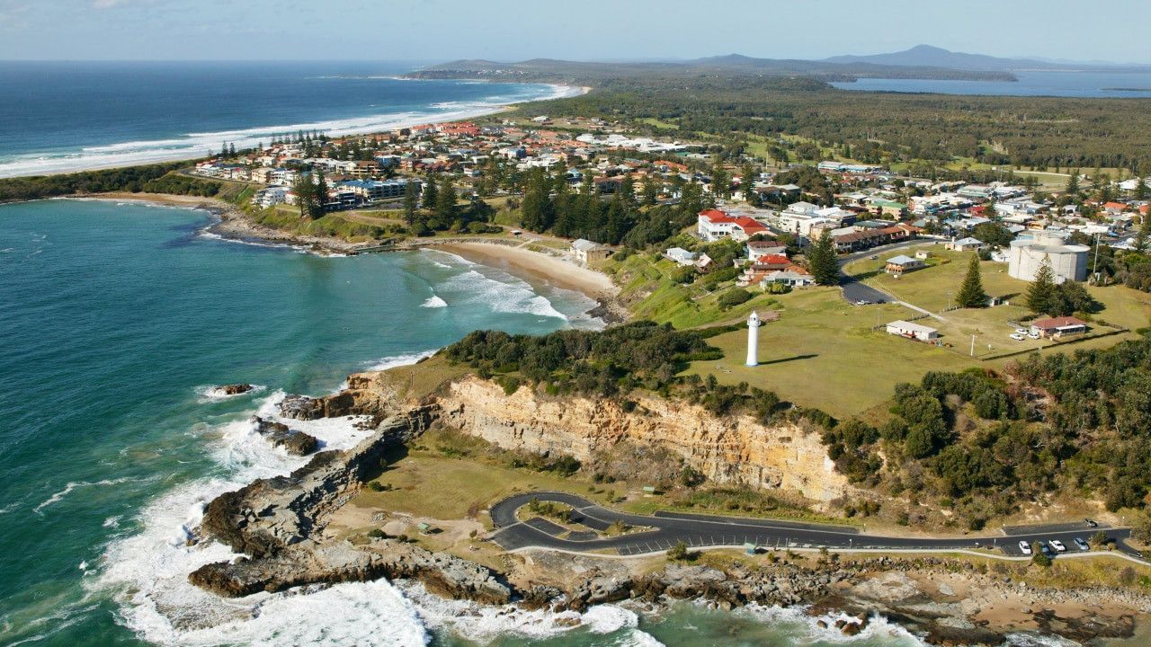 Aerial view of a coastal town with a lighthouse on a cliff overlooking the ocean and beach— Yamba Locksmiths in Yamba, NSW